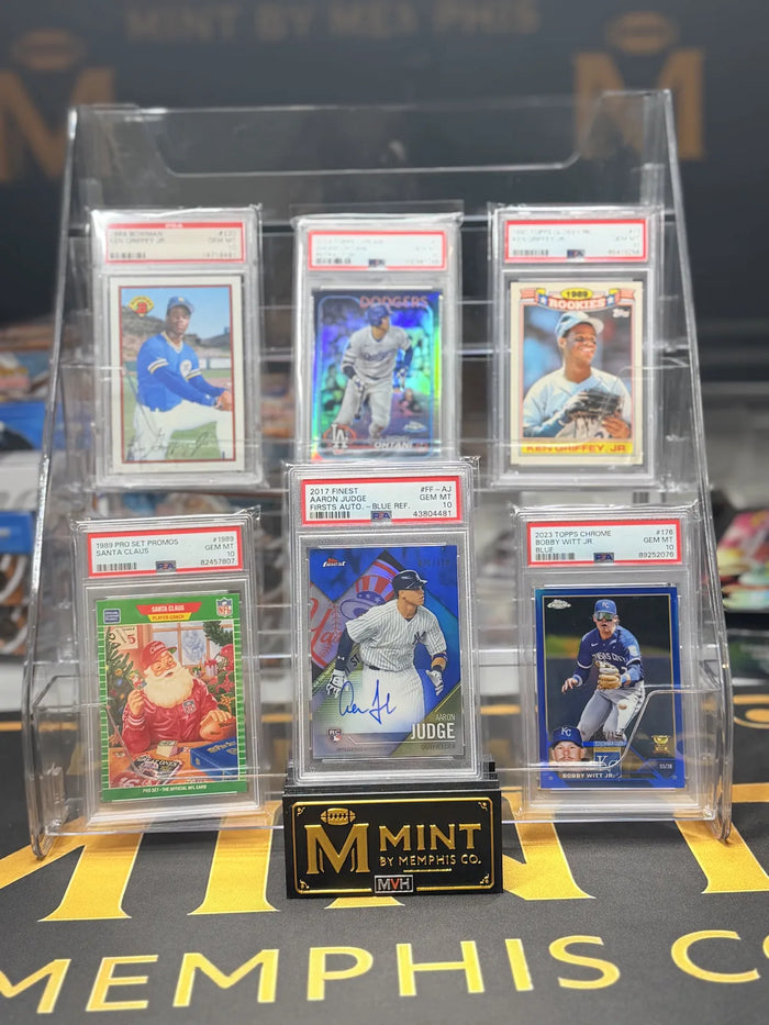 Six PSA 10 graded cards from a newly arrived collection standing in a display riser on the Mint By Memphis mat.