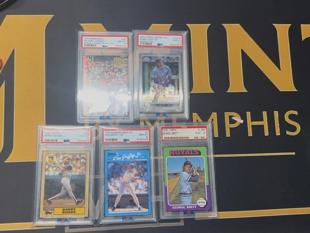 Five PSA graded cards from a recent purchase on the Mint By Memphis mat: a 1992 Upper Deck Michael Jordan error card, a 2022 Topps Chrome Update Bobby Witt Jr. refractor, a 1987 Topps Barry Bonds, and a 1990 Donruss Best Ken Griffey Jr., all PSA 10, with a 1975 Topps George Brett rookie card in PSA 9.
