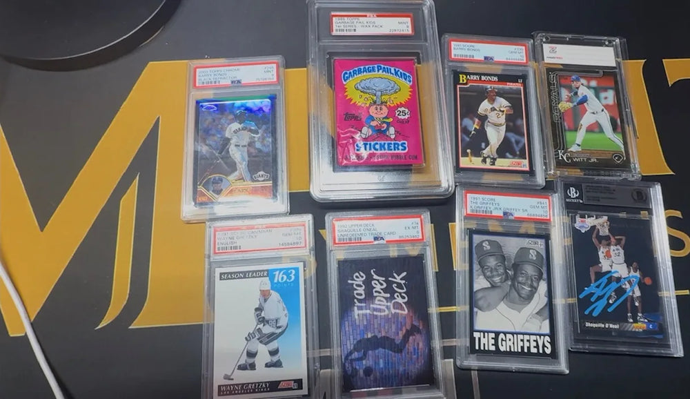Seven graded baseball, basketball and hockey cards and a graded Garbage Pail Kids wax pack from a newly arrived collection, laid out on the Mint By Memphis mat.