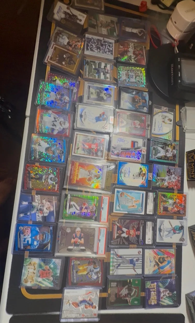 A large multi-card submission of football and basketball cards, many of them autographs and numbered parallels in magnetic holders and graded slabs, laid out on a table.